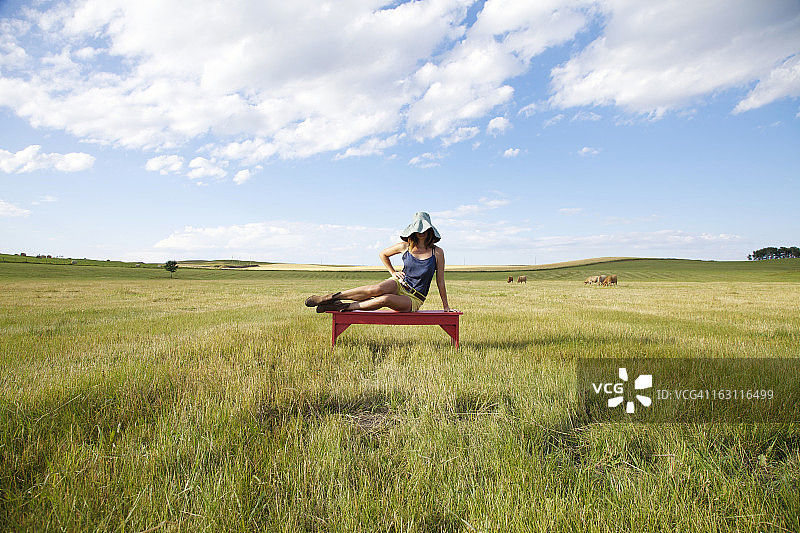 女人躺在绿色草原田野的红色长椅上图片素材