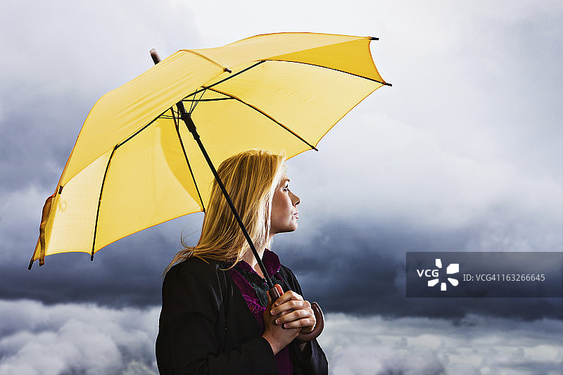 暴风雨天气：忧郁的金发女郎拿着黄色雨伞等待雷暴图片素材
