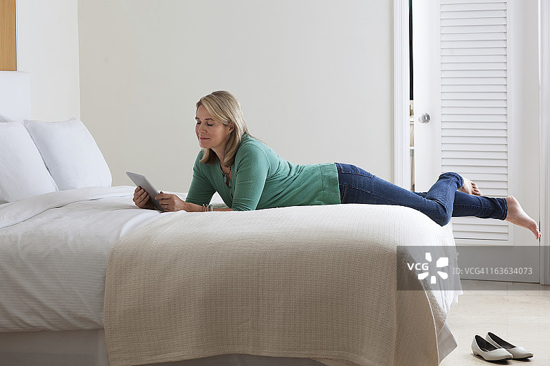 女人躺在床上使用平板电脑图片素材