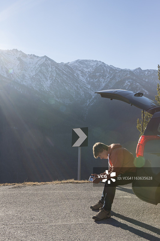 年轻男人在汽车后挡板上使用平板电脑图片素材