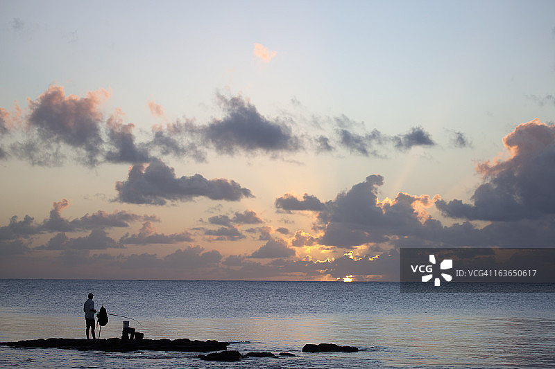 站在毛里求斯大湾村日落时分岩石上的钓鱼男人图片素材
