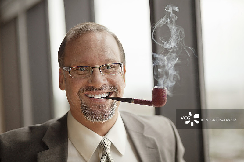 在办公室抽烟斗的年长的商人图片素材