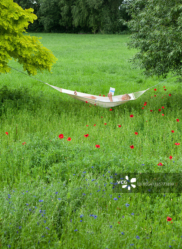 中年妇女躺在花园吊床上看书图片素材