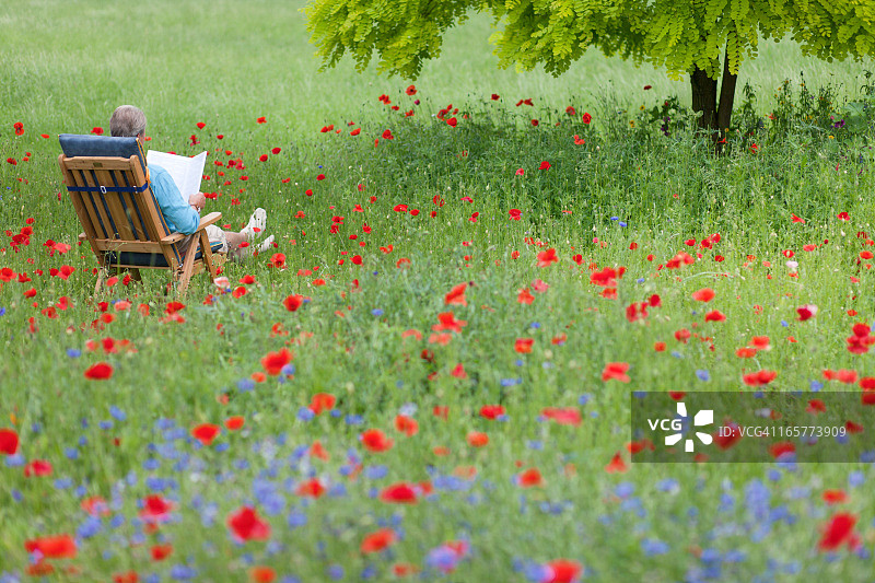 年长的男人躺在花园的躺椅上看书图片素材