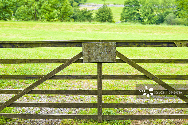 绿色田野中带有空白标志的木栅栏门图片素材