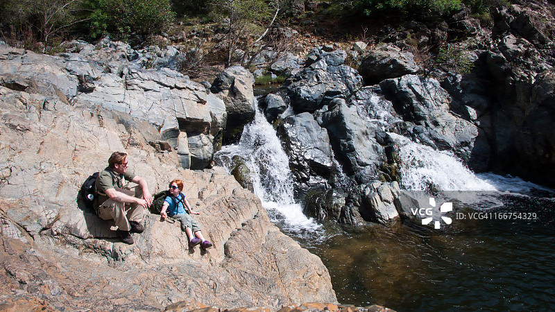 父女坐在瀑布边的岩石上图片素材