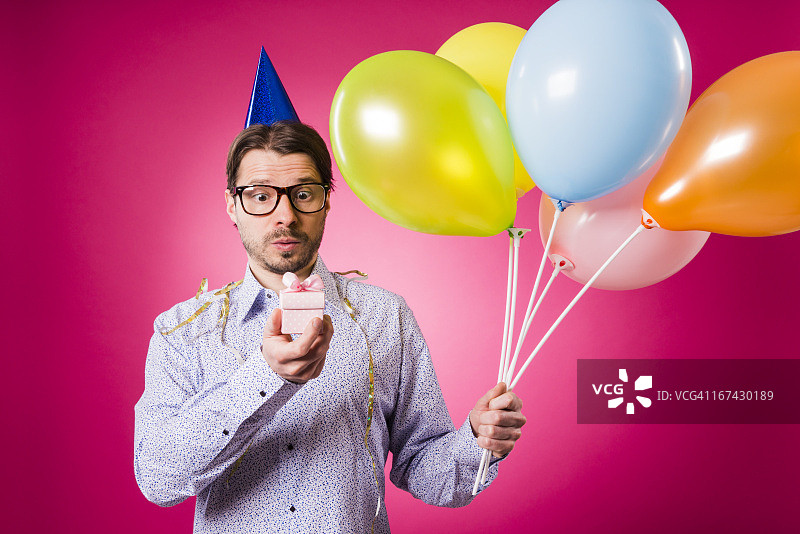 拿着粉色礼物和五个气球的极客男人，生日快乐！图片素材