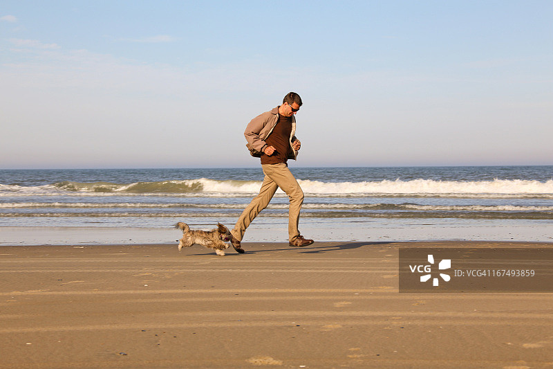 男人和小狗在海边跑步图片素材