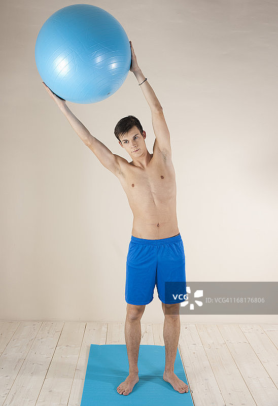 年轻男子用体操球在体操垫上做体操图片素材