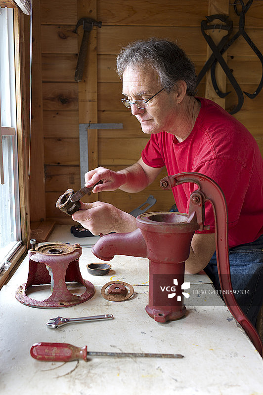 年长男子修理古董手压水泵图片素材