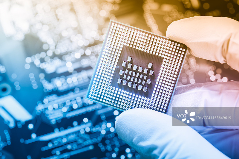 技术员手持芯片，背景是虚化的电路板图片素材