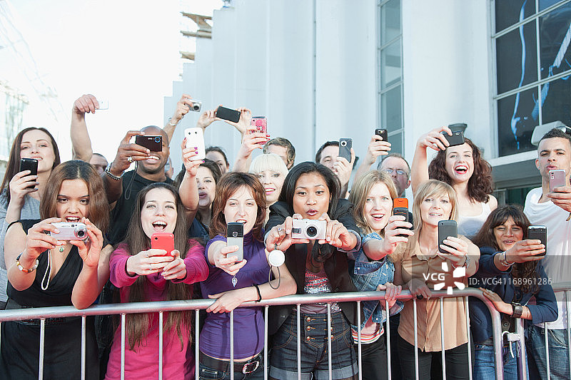 粉丝在屏障后面用手机拍照图片素材