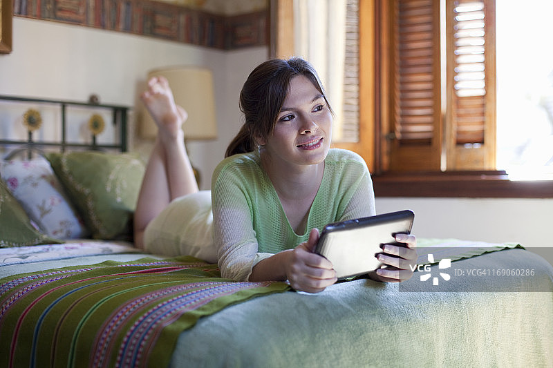 年轻女人躺在床上使用平板电脑图片素材