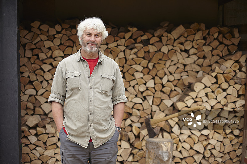 男人站在堆满原木的木棚前图片素材