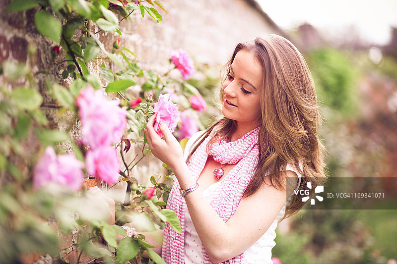 在围墙花园里手持粉色英国玫瑰的女孩图片素材