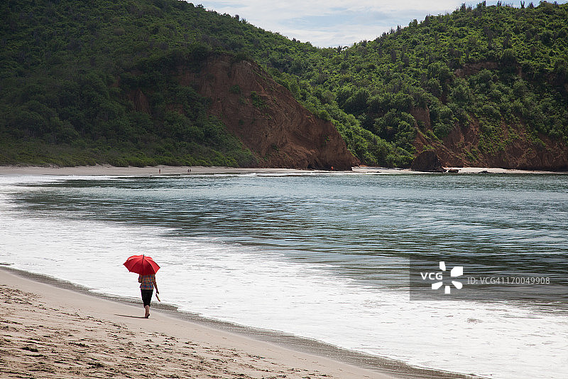 在洛斯弗拉伊莱斯海滩撑红伞的女人图片素材