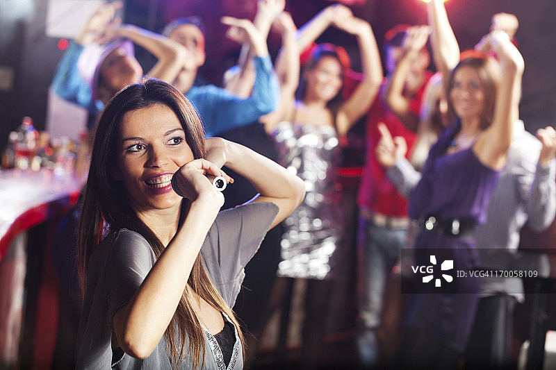 在俱乐部用麦克风唱歌的漂亮棕发女人图片素材