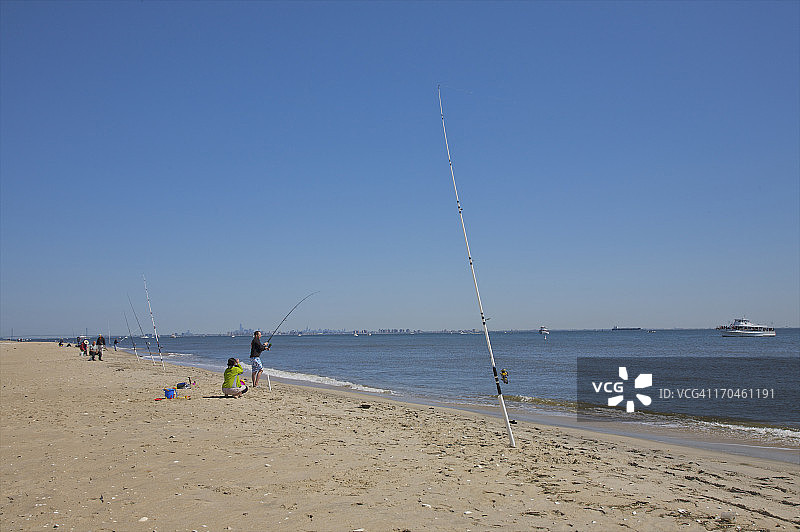 沙滩、海岸线、水中钓鱼的人、蓝天图片素材
