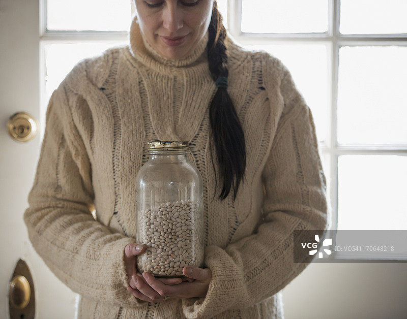 美国纽约州冬季的有机农场，一位女士身穿绞花针织毛衣，手持一罐白豆图片素材