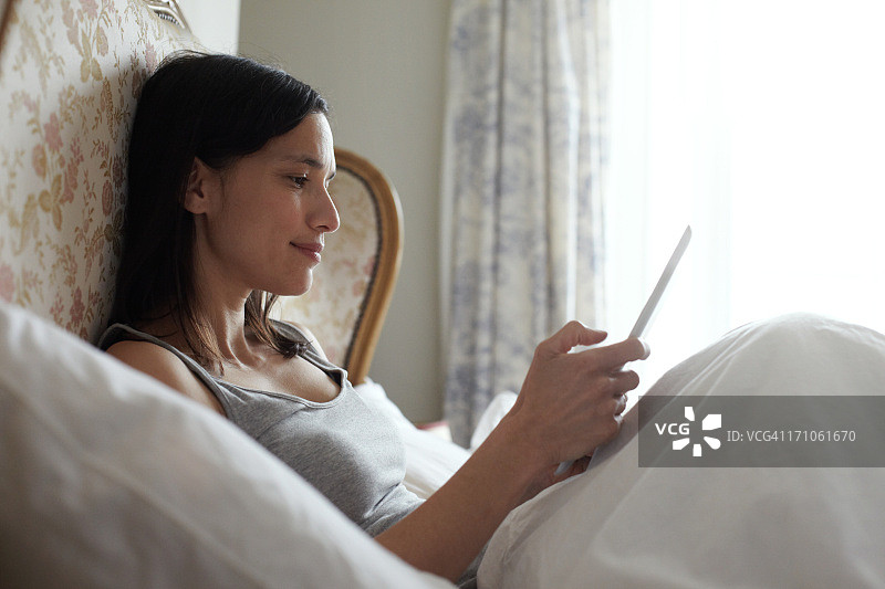 女人坐在床上使用平板电脑图片素材