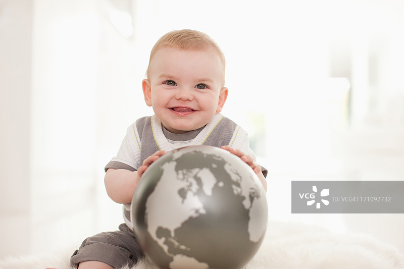 抱着地球仪在地上微笑的婴儿图片素材