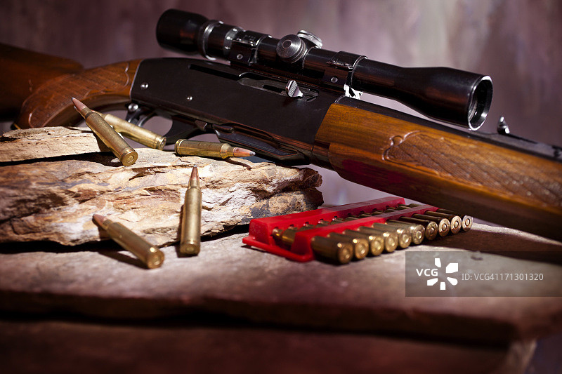 带瞄准镜和弹药的步枪，置于岩石架上图片素材