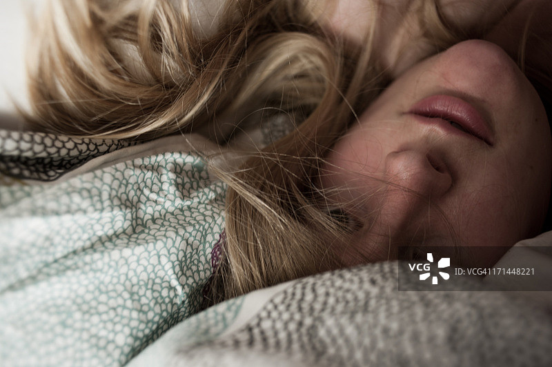 一个金发女人躲在床单下。图片素材