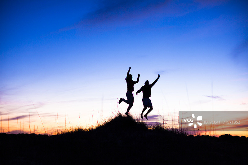 日落时分在海滩上跳跃的两个男人剪影图片素材