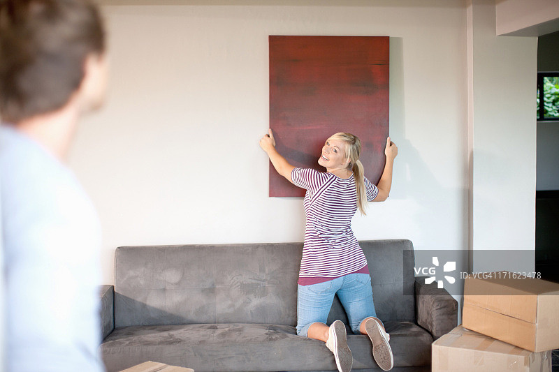 年轻夫妇搬家，妻子挂画图片素材