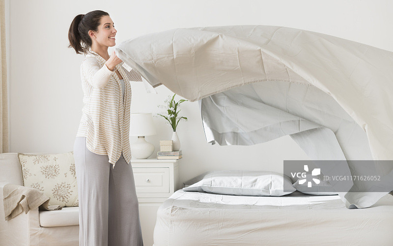 美国新泽西州泽西市：女人在床上铺床单图片素材