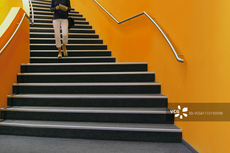 走下橙色楼梯，读书的年轻女子图片素材