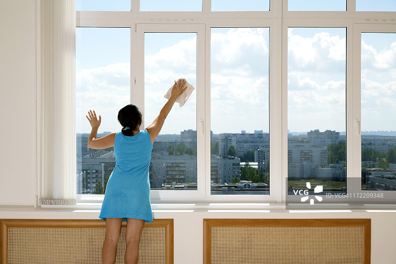 穿着蓝色连衣裙的女人清洁高窗户图片素材
