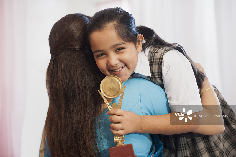 女人拥抱拿着奖杯微笑的女儿图片素材