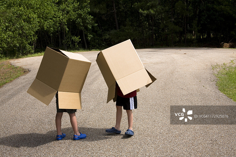 外面有两个男孩，拿着大纸箱盖着身体。图片素材