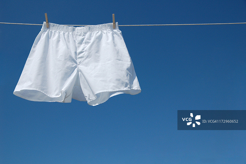 蓝色天空背景下晾衣绳上夹着的白色拳击短裤图片素材