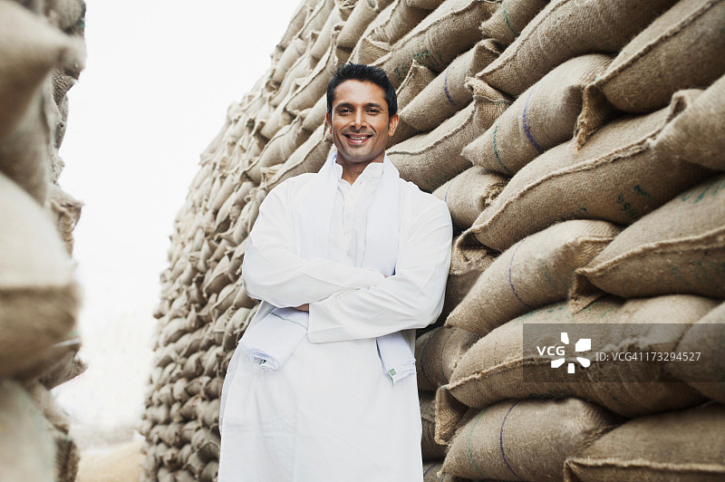 男人站在印度哈里亚纳邦古尔冈索纳Anaj Mandi仓库里的一堆麦袋旁图片素材