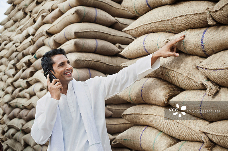男人站在麦袋旁，在印度哈里亚纳邦古尔冈索纳的Anaj Mandi用手机交谈图片素材