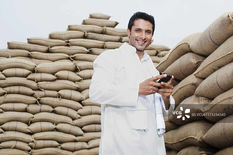 站在成堆麦袋旁，手持手机的男人，印度哈里亚纳邦古尔冈索赫纳的阿纳杰曼迪图片素材