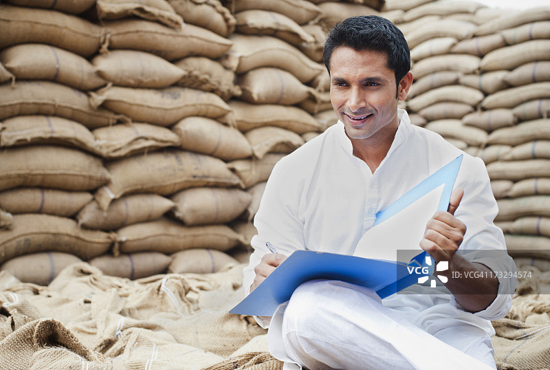 男子坐在麦袋上拿着文件，印度哈里亚纳邦古尔冈索纳图片素材