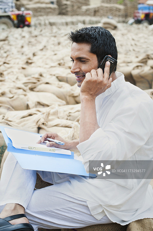 在印度哈里亚纳邦索纳谷物市场，男人拿着文件并用手机交谈图片素材