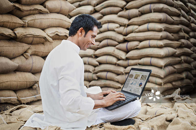 男子坐在印度谷物市场的小麦袋上使用笔记本电脑图片素材