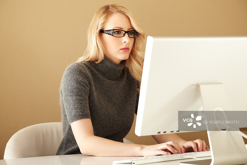 在电脑上打字的迷人金发女人图片素材