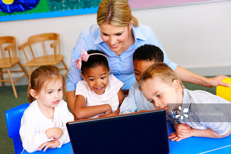 幼儿园里，美丽的老师和使用笔记本电脑的学生们图片素材