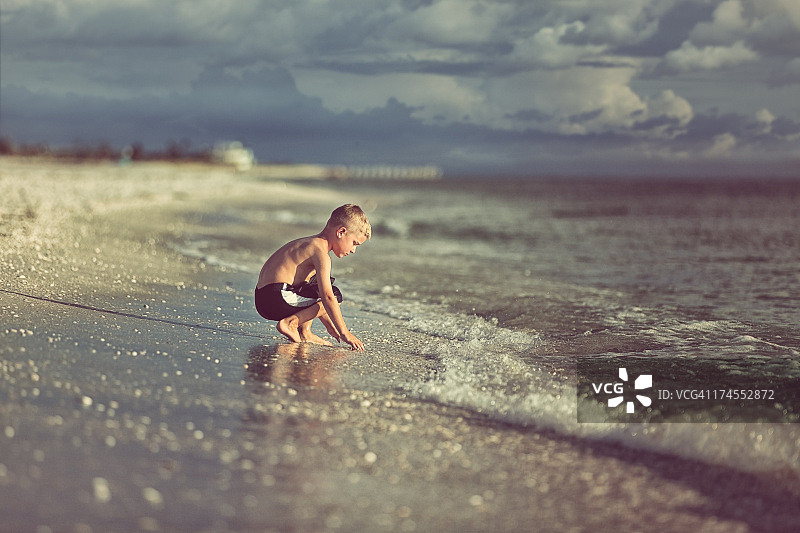 男孩在墨西哥湾前的沙滩上蹲着图片素材