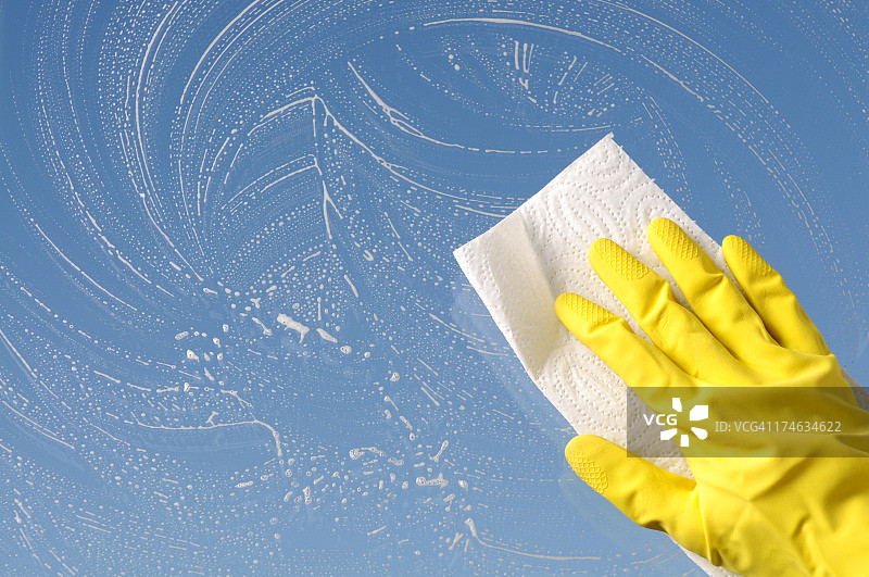 戴黄色防护手套的手清洁窗户，天空背景图片素材
