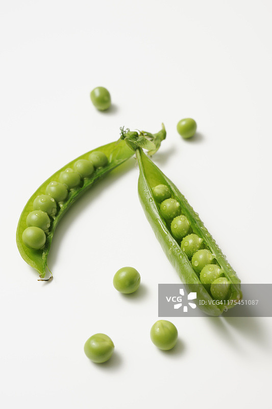 白色背景上带水珠的已打开的新鲜青豌豆图片素材