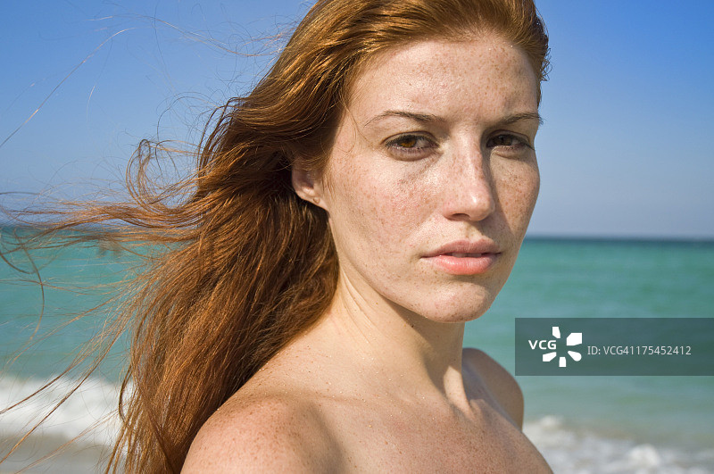 海滩上的红色长发女子（未穿上衣，表情严肃）图片素材