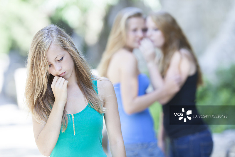 背景中朋友窃窃私语的悲伤青少年图片素材
