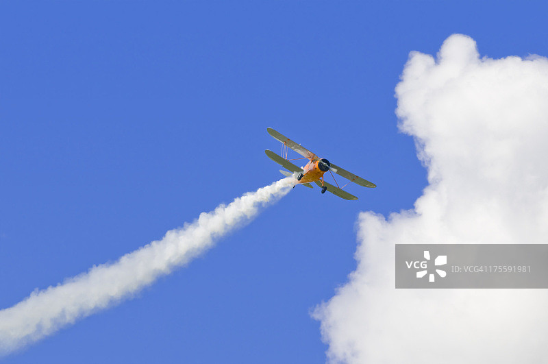 带有蒸汽轨迹、蓝天和白云的双翼飞机图片素材