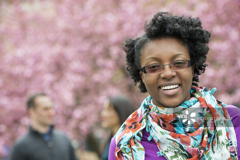 公园里樱花树下的一群人，一位年轻女子面带微笑地看着镜头，戴着花卉围巾图片素材
